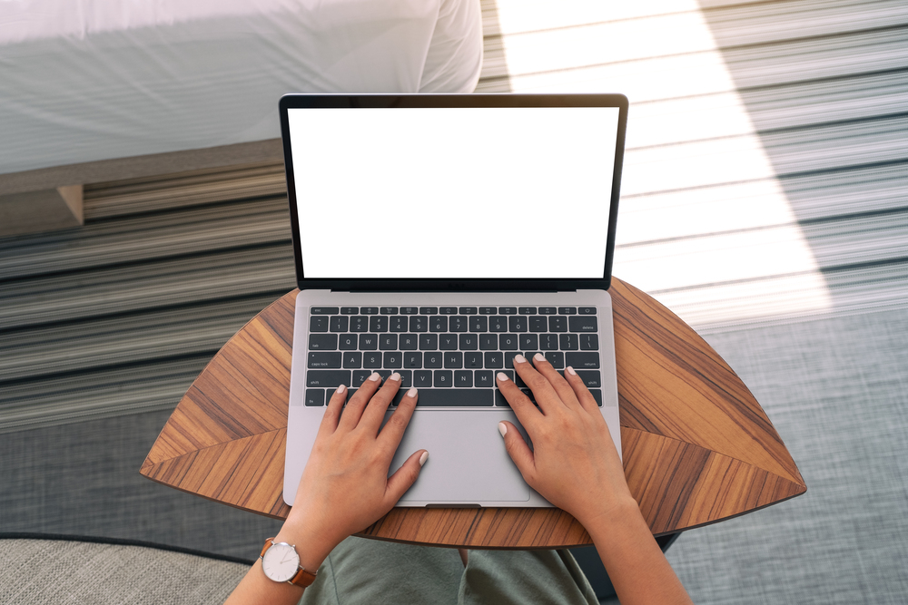 top view mockup image woman using typing laptop with blank white desktop screen keyboard wooden table bed